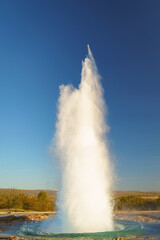 The Strokkur geyser erupting in Haukadalur, Iceland, shooting boiling water into the air under a clear blue sky.