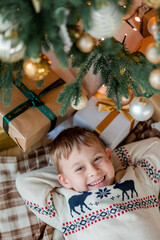 Happy boy open gifts near the Christmas tree. Holidays.