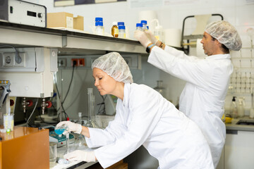 Professional male and female biologists in lab coat examining reaction in test tube while working in research center