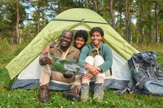 Portrait of African American family holding map and sitting in tent while posing for photo in forest