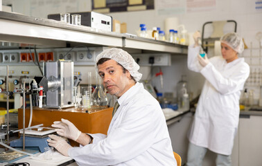 Professional middle-aged male scientist placing substance on stand for examination under microscope in research center