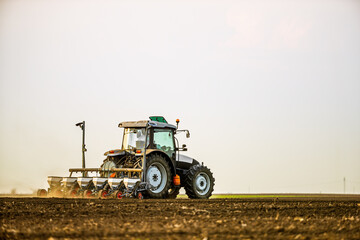 Modern tractor seeding, planting agricultural field at dusk