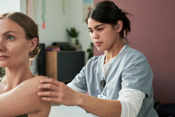 Medical professional wearing scrubs attentively administering injection to patient in clinical setting Foreign objects in background indicating medical environment