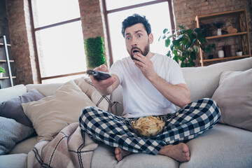 Photo of crazy terrified young man in pajamas enjoying weekend at home watching movie living room indoors