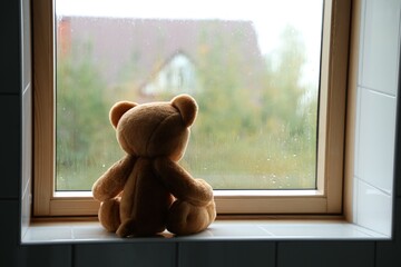 Lonely teddy bear near window on rainy day. Space for text