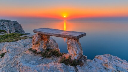A wooden bench sits atop a cliff overlooking the ocean as the sun sets on the horizon.
