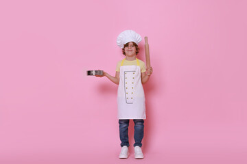 Little boy with utensils pretending to be chef on pink background. Dreaming about future profession