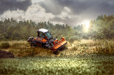 Fototapeta premium traktor mit rasenmäher schneidet hohes gras an einem hügel mit grünen gras im vordergrund und strahlendem sonnenschein