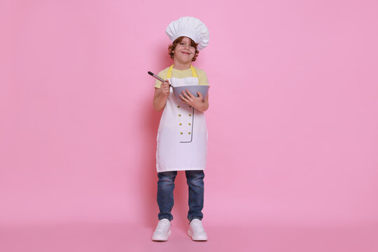 Little boy with bowl and whisk pretending to be chef on pink background. Dreaming about future profession