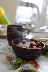 Sweet dumplings (vareniki) garnished with frozen raspberries, served in a rustic wooden bowl. The cozy setting highlights the dish's warmth, ideal for food photography or traditional dessert concepts