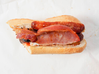 Traditional Irish breakfast roll with cooked sausages, bacon or rashers and black and white pudding in a round bread on light color paper. Popular meal with high calorie count.