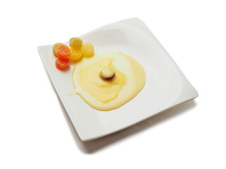 Condensed milk and custard desert looks like a fired egg and colorful jelly sweets in sugar on a white fancy square plate and light background. Creative food ideas. Light and airy look