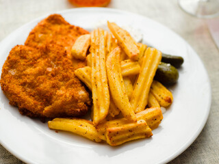Breaded chicken fillet meal and fried potatoes chips with ridges on a white plate and light color table cloth. Simple food made of high quality premium products. Cooked poultry meat.