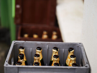 A crate full of beer or cider bottles with gold foil rim on them. The crate is by a wall. Party...