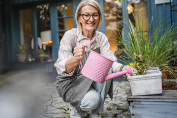 Fototapeta premium Mature woman waitress waters plants in garden with a pink watering can
