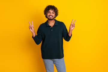 Cheerful young man posing in black shirt on vibrant yellow background, promoting energy and positivity