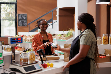 African American vendor serves a customer at a checkout counter using a debit card for wireless...