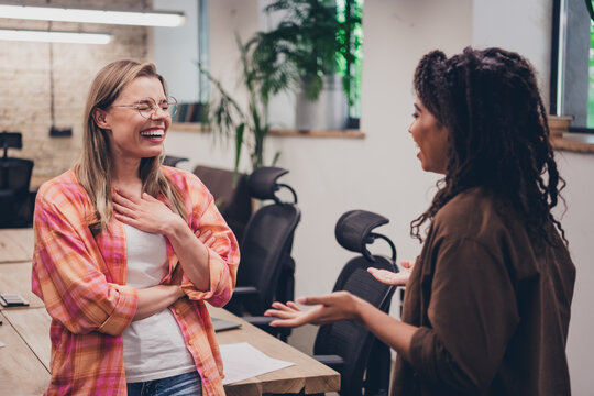Photo of two ambitious businesswomen coworking chatting tell joke laugh modern loft interior office indoors