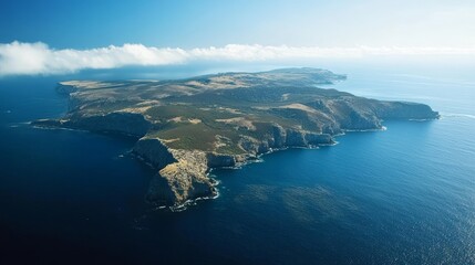 Aerial view of a scenic island with rugged coastline, lush vegetation, and clear blue ocean under a bright sky.