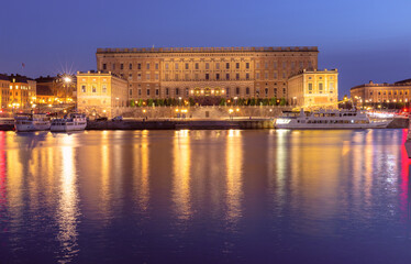Obraz premium The Royal Palace in Stockholm, illuminated at sunset, is reflected in the calm waters of the Gulf of Stockholm, Sweden.