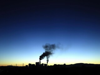 Smoldering cityscape at dusk with dark smoke hanging low, smoke and flames, smoky sky