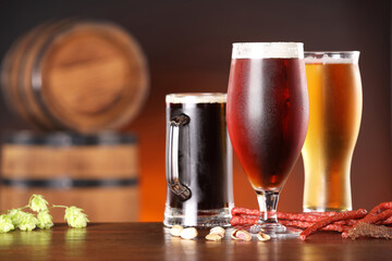Glasses with different types of beer, snacks and fresh hops on wooden table in bar. Space for text