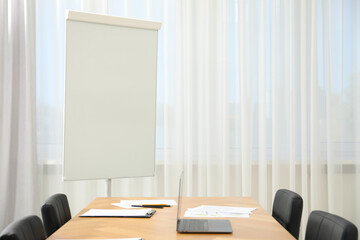 Flip chart, wooden table and chairs in conference room. Mockup for design