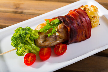 Grilled quail with jamon, fried on skewers with brocolli and tomatoes at plate
