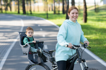 Obraz premium Caucasian woman riding a bicycle with her toddler son sitting behind her in a child seat. 