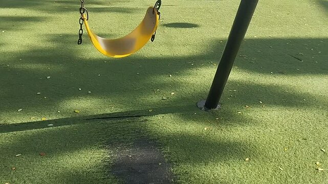 An empty yellow swing moving back and forth in a playground.