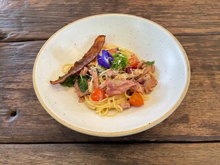 Spicy and herbs spaghetti with hams and beacons in white ceramic dishes on wooden table