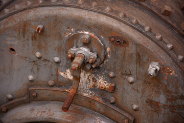 An old mechanical machine used for controlling a thermal spring. The weathered brass components and complex gears highlight its vintage design. The background features natural stone textures.