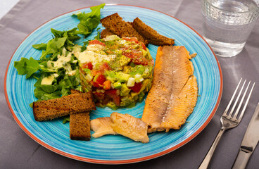 Image of tasty salad guacamole with arugula and tomatoes aerved with grilled trout fillet at plate