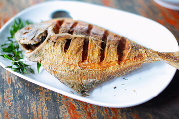 Crispy fried cotton fish placed on a white plate on a wooden table, close-up photo.