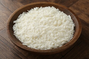 White soy wax flakes in bowl on wooden table, closeup