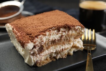 Piece of tasty tiramisu and fork on black table, closeup