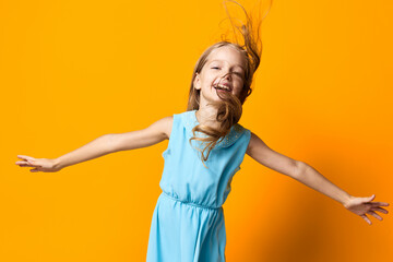 Joyful little girl in blue dress with outstretched arms against a vibrant orange background