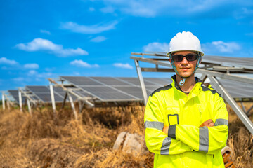 A confident solar energy technician, wearing a helmet and reflective jacket, stands with arms crossed in front of an array of photovoltaic panels, under a bright and clear blue sky.