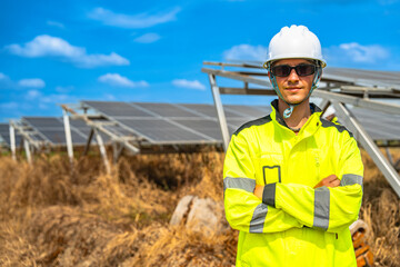 A confident solar energy technician, wearing a helmet and reflective jacket, stands with arms crossed in front of an array of photovoltaic panels, under a bright and clear blue sky.