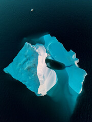 drone shot of a huge iceberg  and a small boat in dark arctic waters, Greenland