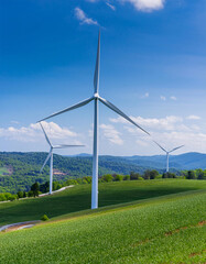 Wind turbines on a green hill with a road winding through it and mountains in the background