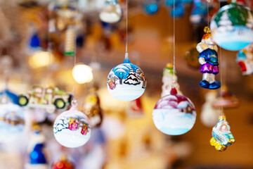 Variety of hand-painted Christmas ornaments, including baubles and figurines, hang from strings in festive market setting, beautifully lit by warm lights