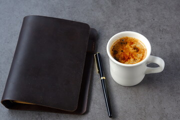 ミルクを入れたコーヒー、カフェ・ラッテを飲みながら、茶色の革のシステム手帳でデスクワーク中のイメージ
