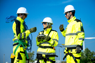 An engineer in a hard hat and safety vest operates a drone to inspect towering wind turbines in a remote area.