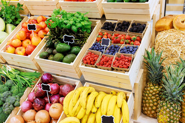 Colorful selection of fresh produce including berries, bananas, greens showcased in wooden crates...