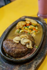 A close-up of a thick, juicy beef steak and fluffy roasted potatoes on a hot plate. The contrast between the red meat, golden potatoes, and green herbs creates a visually appealing dish.