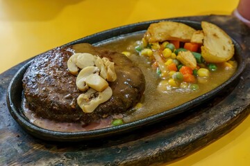 A close-up of a thick, juicy beef steak and fluffy roasted potatoes on a hot plate. The contrast between the red meat, golden potatoes, and green herbs creates a visually appealing dish.