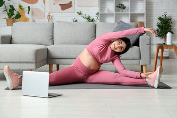 Sporty young pregnant woman stretching in living room