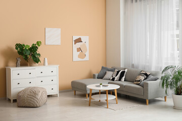 Chest of drawers, cozy sofa, coffee table and picture hanging on beige wall in living room