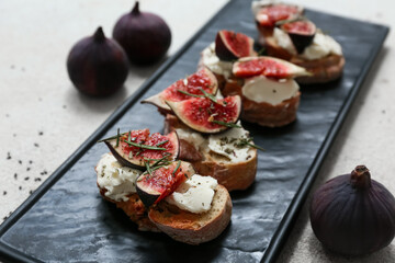 Black board of delicious fig bruschetta with ricotta cheese and rosemary on white background, closeup